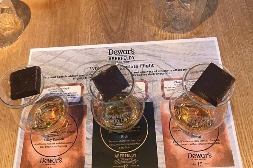 Trois petits verres à whisky remplis de whisky Dewar's Ardfelda, chacun accompagné d'un morceau de chocolat. 4