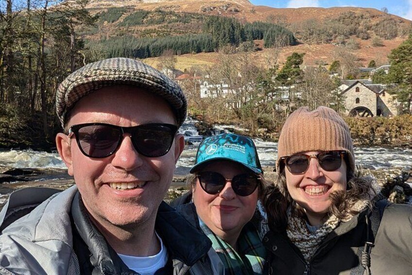 Three people outdoors with a river and buildings in the background. 4