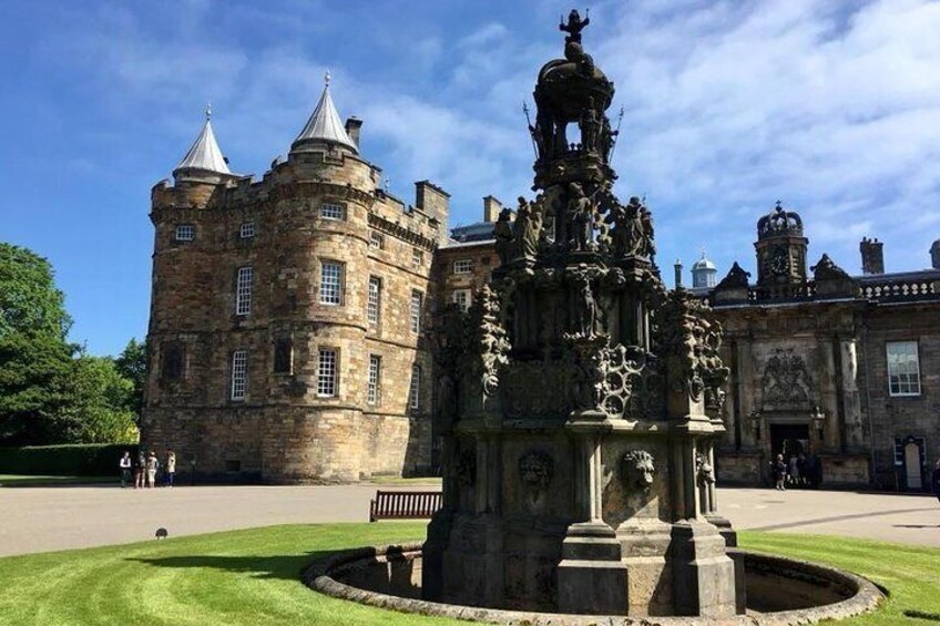 A historic stone building with a turreted tower and a fountain with statues. 4