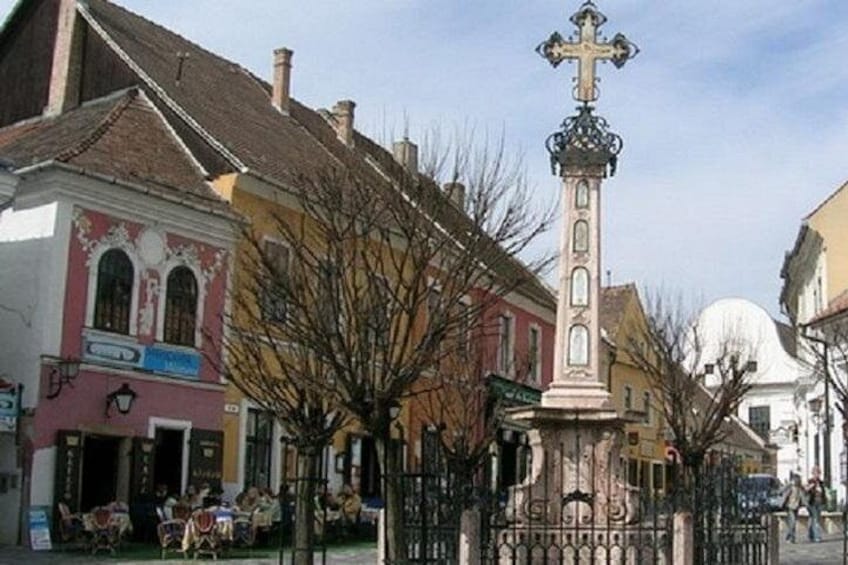 Une rue bordée d’immeubles, un monument en forme de croix et des arbres sans feuilles. 3
