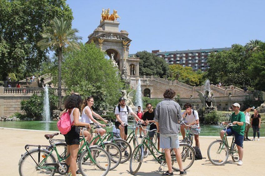 A group of people on bicycles in a park with fountains and a historic building in the background. 2