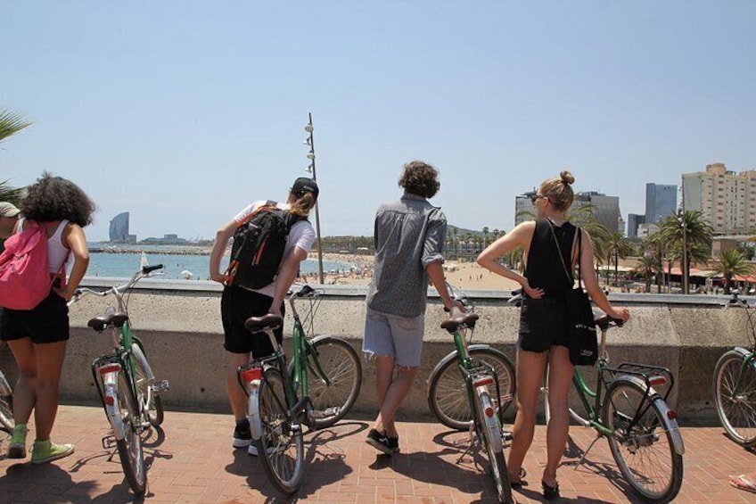 Des personnes se tiennent sur une promenade, à côté de leurs vélos, et contemplent une plage ainsi que le paysage urbain. 2