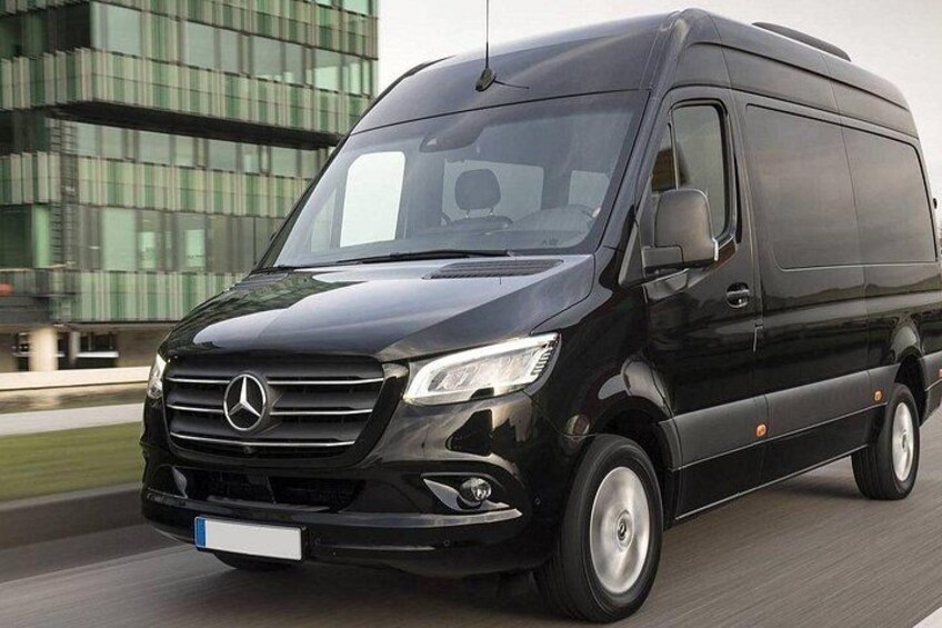 A black Mercedes van driving on a road with a modern building in the background. 2