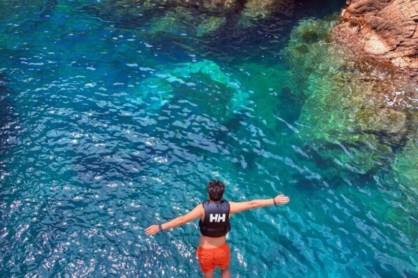 Una persona de pie en aguas cristalinas y azules, con los brazos extendidos, vistiendo una blusa negra y pantalones cortos rojos. 4