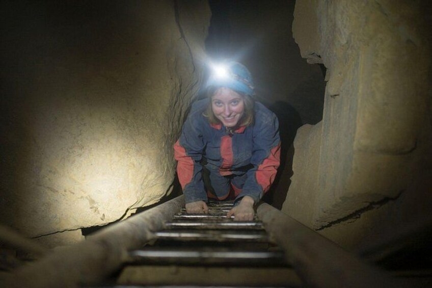 A person climbing a narrow, rocky path with a headlamp. 1