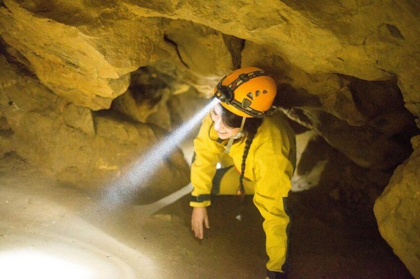 Une personne vêtue d’une combinaison jaune et portant un casque explore une grotte à l’aide d’une lampe de poche. 2