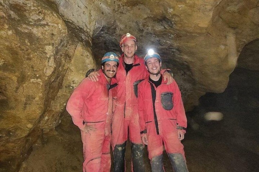 Three people in a cave wearing red jackets and helmets. 5