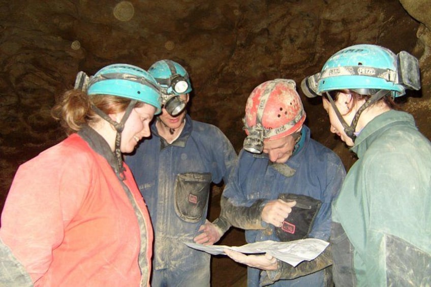 People in helmets and work clothes in a cave, examining a map. 3