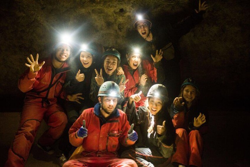 Un groupe de personnes vêtues d’uniformes rouges et portant des casques, dont certaines tiennent des lampes, se trouve dans une grotte faiblement éclairée. 3