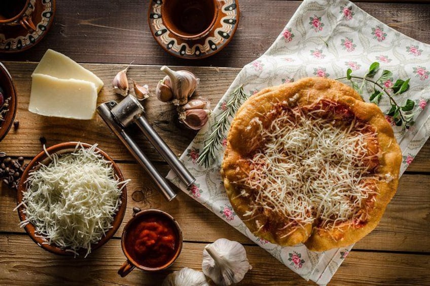 Une pizza à la mozzarella et à la sauce tomate, entourée d’ail, de romarin et d’une râpe, le tout posé sur une table en bois. 4