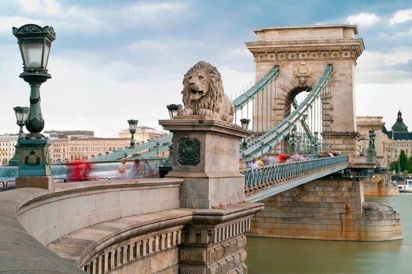 Een stenen brug met een standbeeld van een leeuw, een hangbrug en een rivier. 4