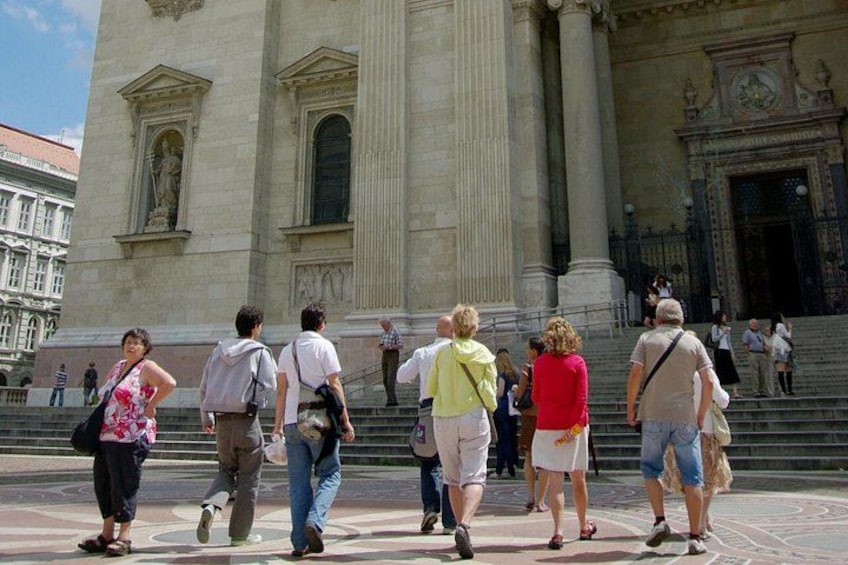 Un groupe de personnes marchant devant un grand bâtiment de style classique, orné de colonnes et de statues. 5