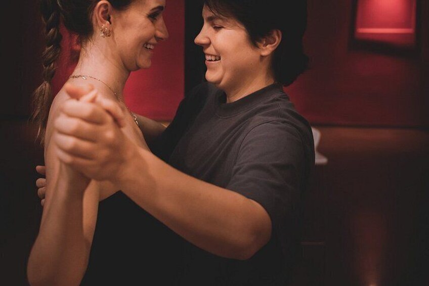 Two people holding hands, possibly dancing, in a dimly lit room with a red wall. 4