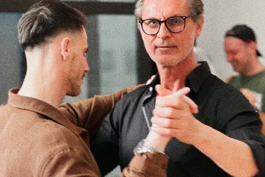 Two people in a room, one wearing a brown shirt and the other in a black shirt, holding hands. 3