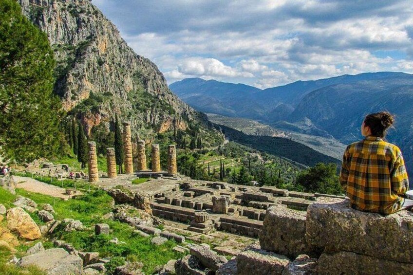Ruinas antiguas con columnas, una persona sentada sobre una roca y un paisaje montañoso al fondo. 3