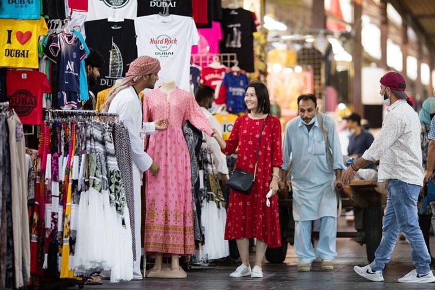 Un marché animé où l’on peut voir des gens faire leurs emplettes, des étalages de vêtements et une pancarte sur laquelle on peut lire : « J’adore DUBAÏ ». 5