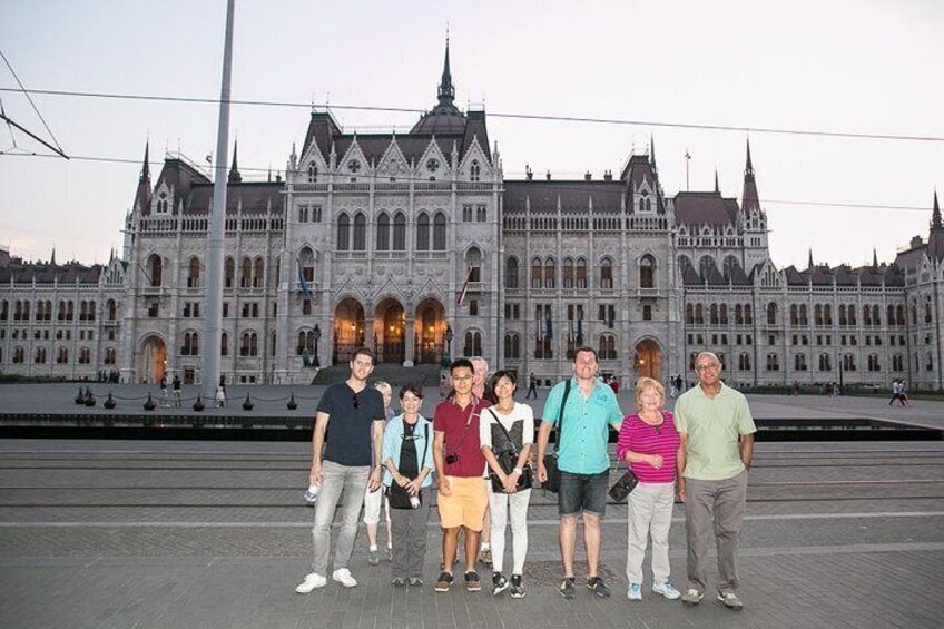 A group of people standing in front of a large, ornate building with multiple towers and a central dome. 1