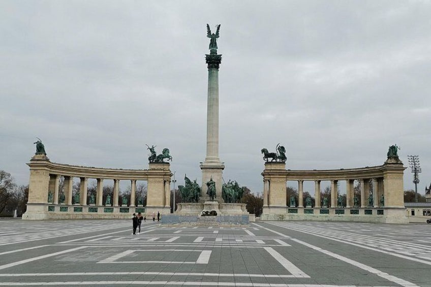 Une vaste place publique, ornée d’un monument central, et bordée de deux bâtiments symétriques surmontés de statues. 5