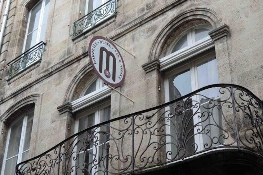 A building with a wrought iron balcony and a sign with a letter 'M' on it. 1