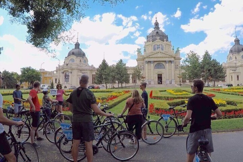 Un grupo de personas con bicicletas en un parque con jardines cuidados y arquitectura clásica. 2
