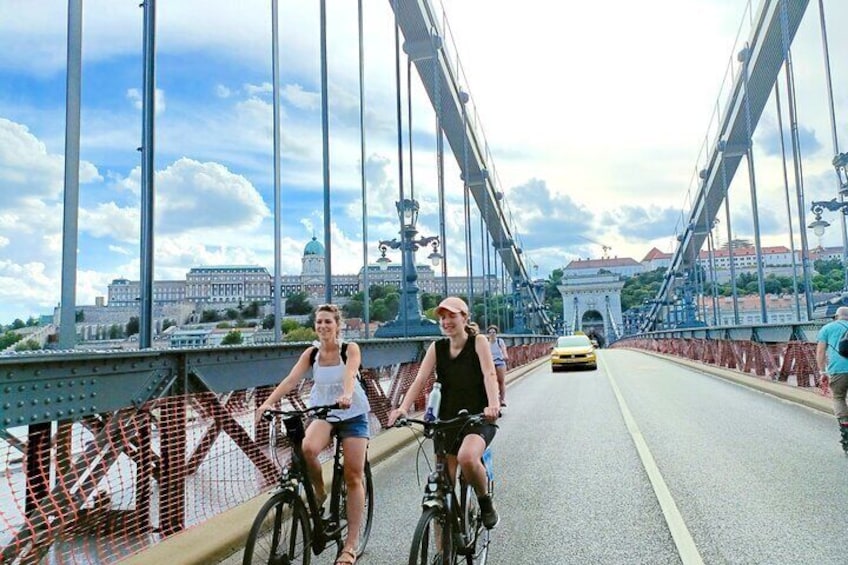 Dos personas andan en bicicleta sobre un puente, con un paisaje urbano al fondo. 4