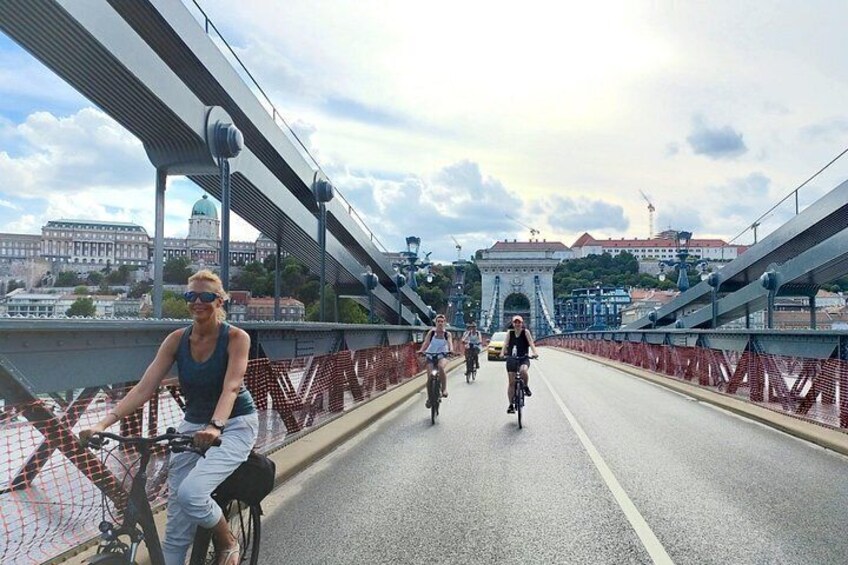 Un puente con ciclistas, una gran estructura en arco y edificios al fondo. 2