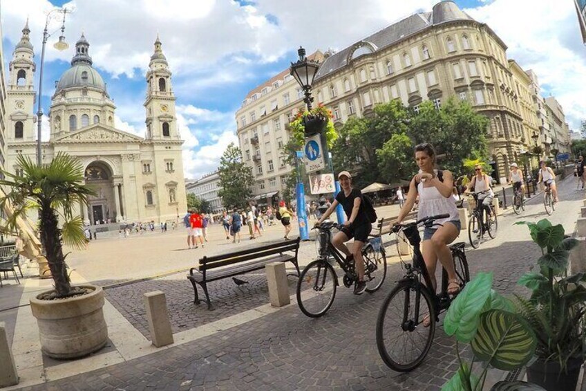 A city square with a large historic building, people walking, and cyclists on the street. 5