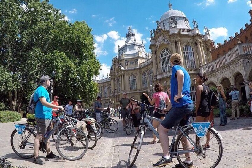 People riding bicycles in a plaza with a historic building in the background. 4