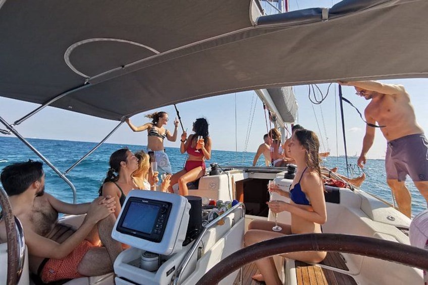 Un grupo de personas en un velero, algunas de pie y otras sentadas, con un timón y un panel de control a la vista. 2
