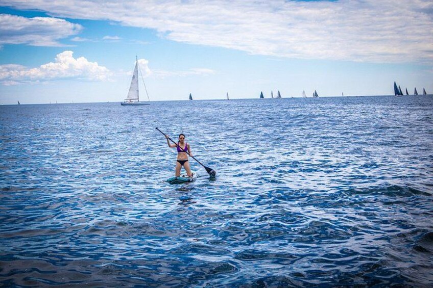 Una persona haciendo paddleboard en aguas oceánicas tranquilas, con veleros a lo lejos. 5