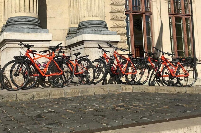 Rækkevis af orange cykler parkeret op ad en bygning med søjler og vinduer. 2