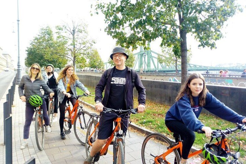 Eine Gruppe von Radfahrern auf einem Uferweg, im Hintergrund eine Brücke. 2