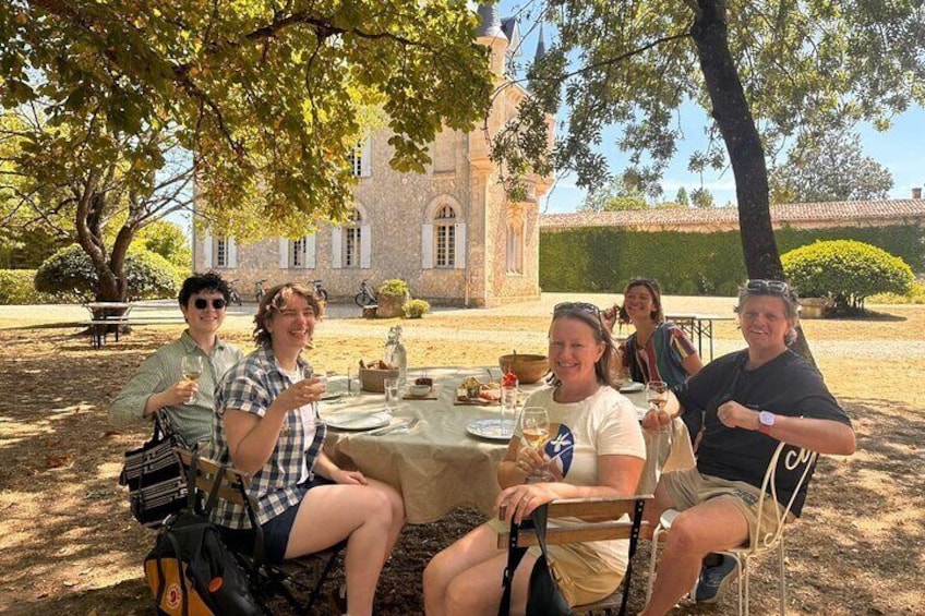A group of people dining outdoors at a table with a building in the background. 2