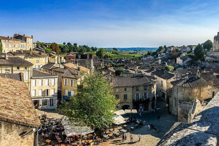 A historic town with stone buildings, a central square, and a view of the countryside. 2