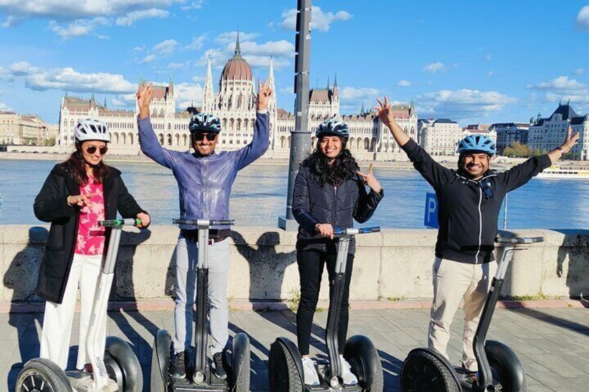 Vier personen op segways voor een historisch gebouw aan een rivier. 4