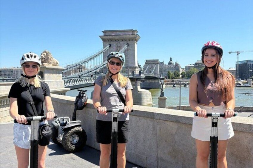 Drie personen op scooters nabij een brug met een standbeeld van een leeuw en water. 2