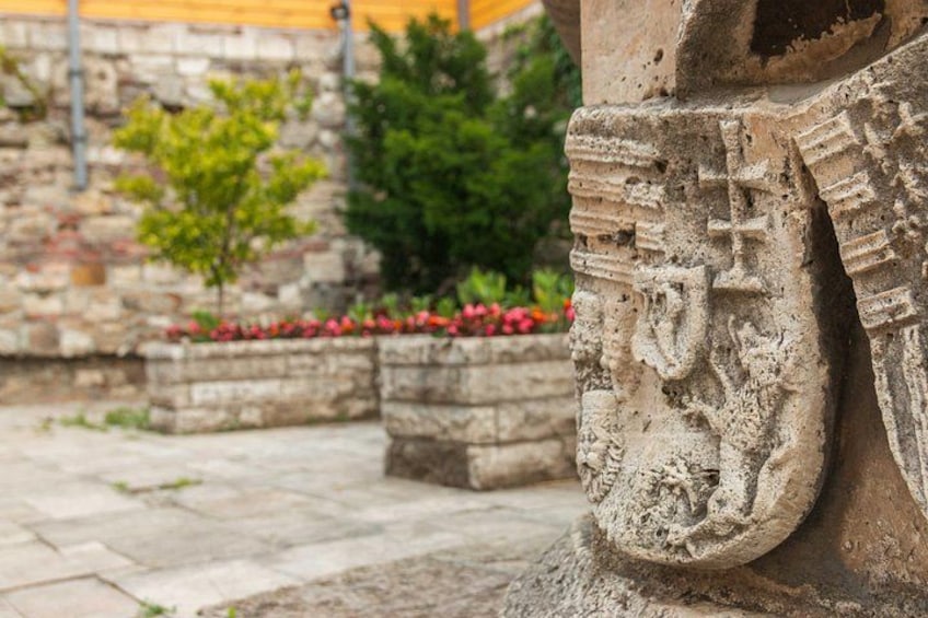 Una struttura in pietra con intagli, un muro di pietra e un piccolo albero con fiori rossi. 1