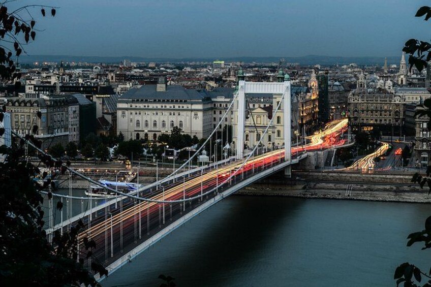 A bridge with light trails, a river, and a cityscape with buildings. 2