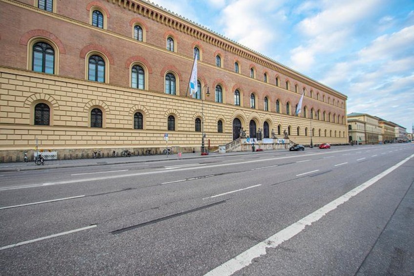 A large, historic building with a red facade and arched windows, located next to a wide, empty road. 4