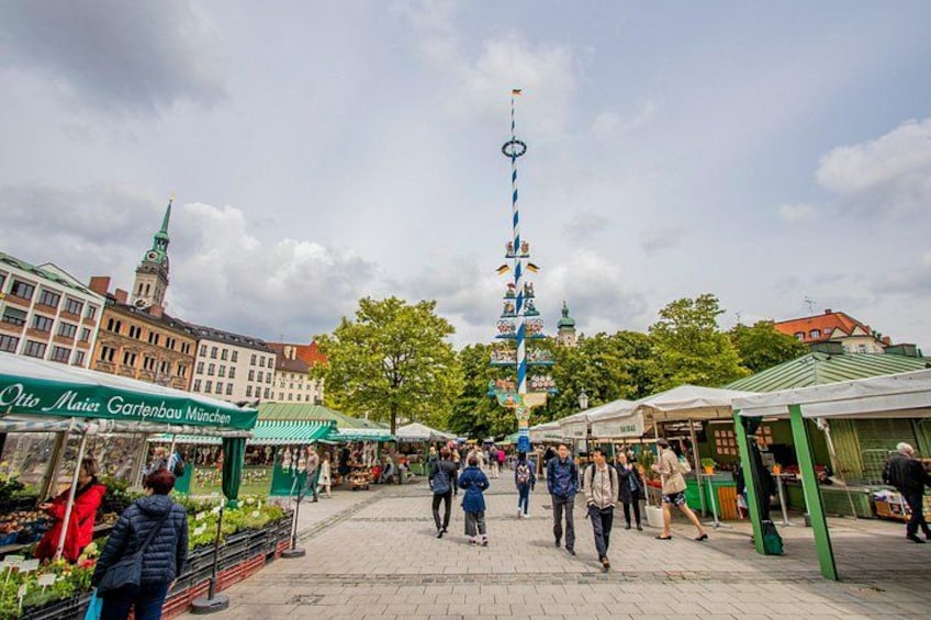 A bustling outdoor market with people walking, stalls selling goods, and a prominent tower in the background. 2