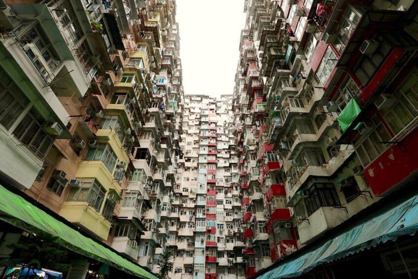 A densely packed residential area with multi-story buildings, balconies, and a narrow street. 1