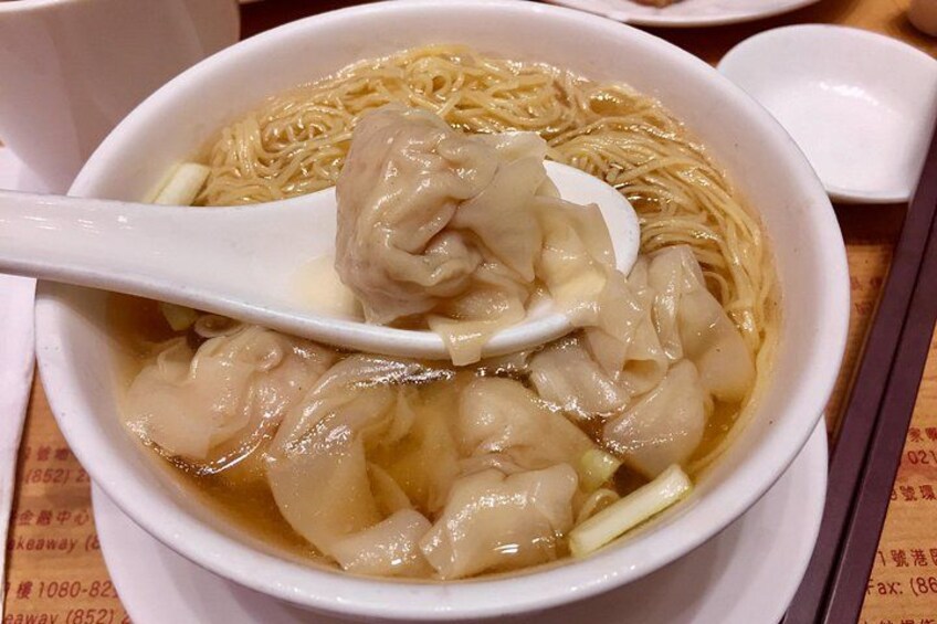 A bowl of noodle soup with dumplings and a white spoon. 3
