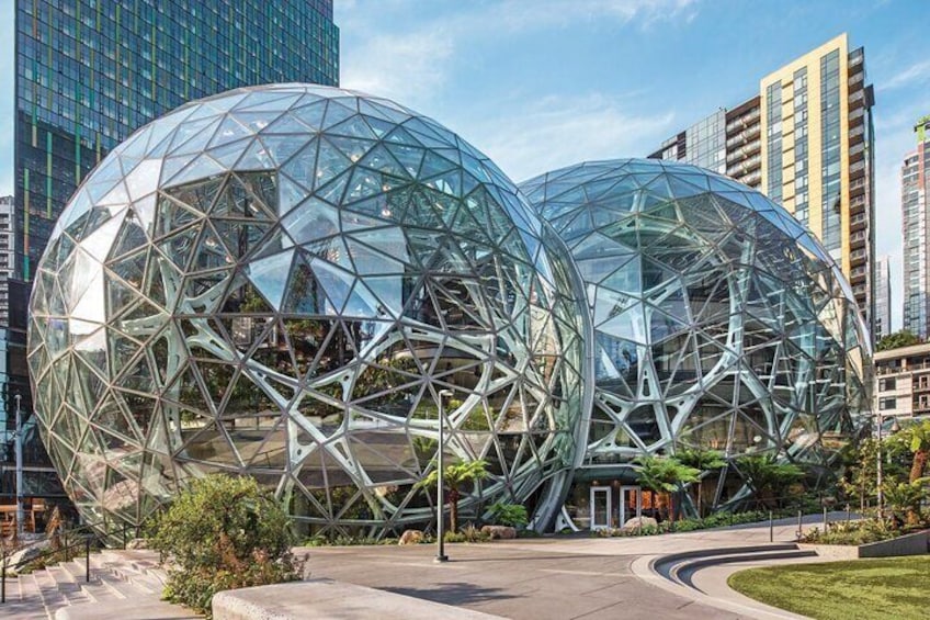 Two large glass domes with a geometric framework, surrounded by urban buildings and greenery. 3