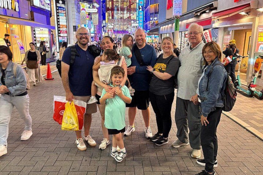 A group of people standing on a city street with shops and signs in the background. 4