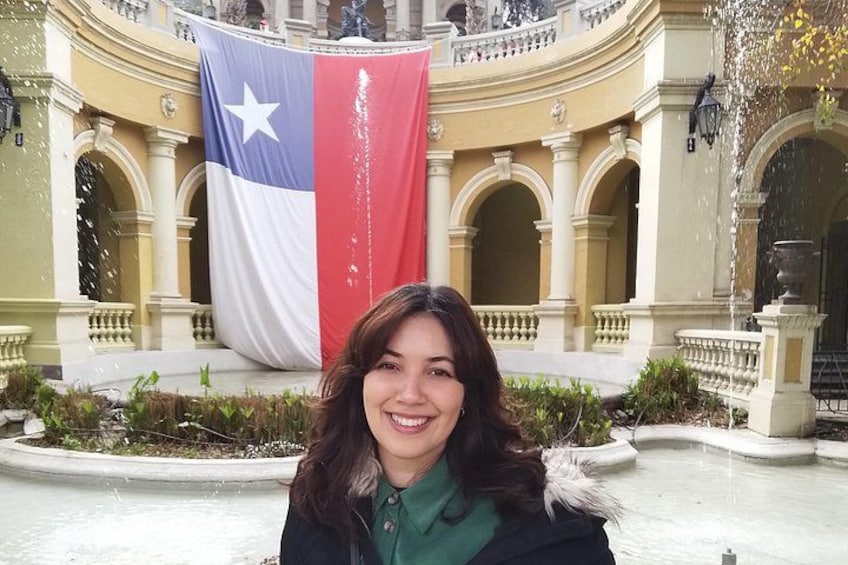 Una persona frente a un edificio con una gran bandera, ventanas arqueadas y una fuente. 5
