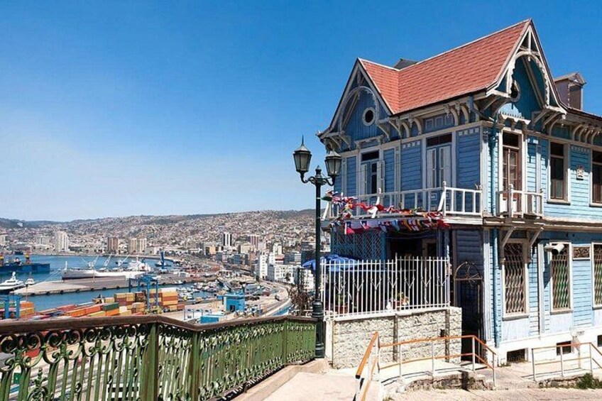 A coastal cityscape with a prominent blue building with a red roof, a harbor with boats, and a clear blue sky. 3