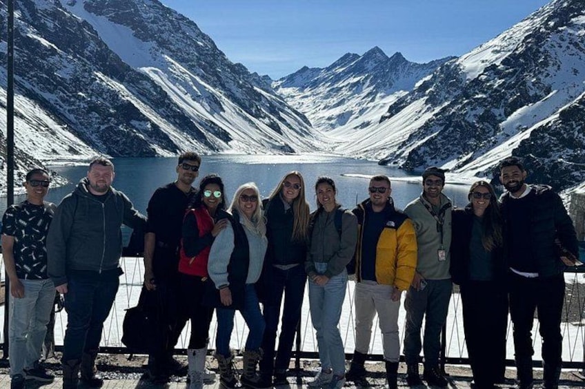 Een groep mensen staat in een bergachtig gebied met besneeuwde toppen en een meer op de achtergrond. 2