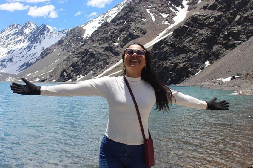 A person standing by a clear blue lake with mountains in the background. 2