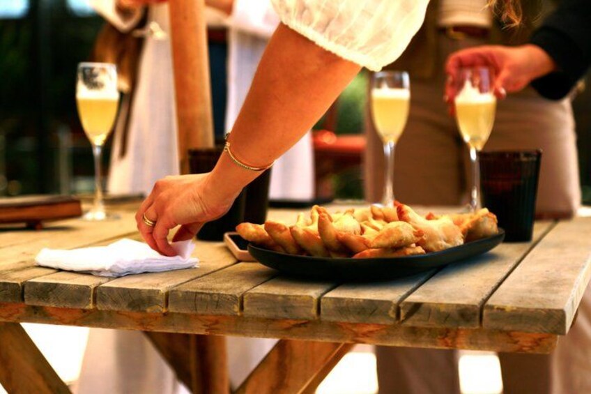 A wooden table with a plate of food and two glasses of a light-colored beverage. 2