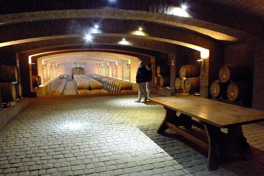 A cellar with wooden barrels, a long table, and a person standing. 2